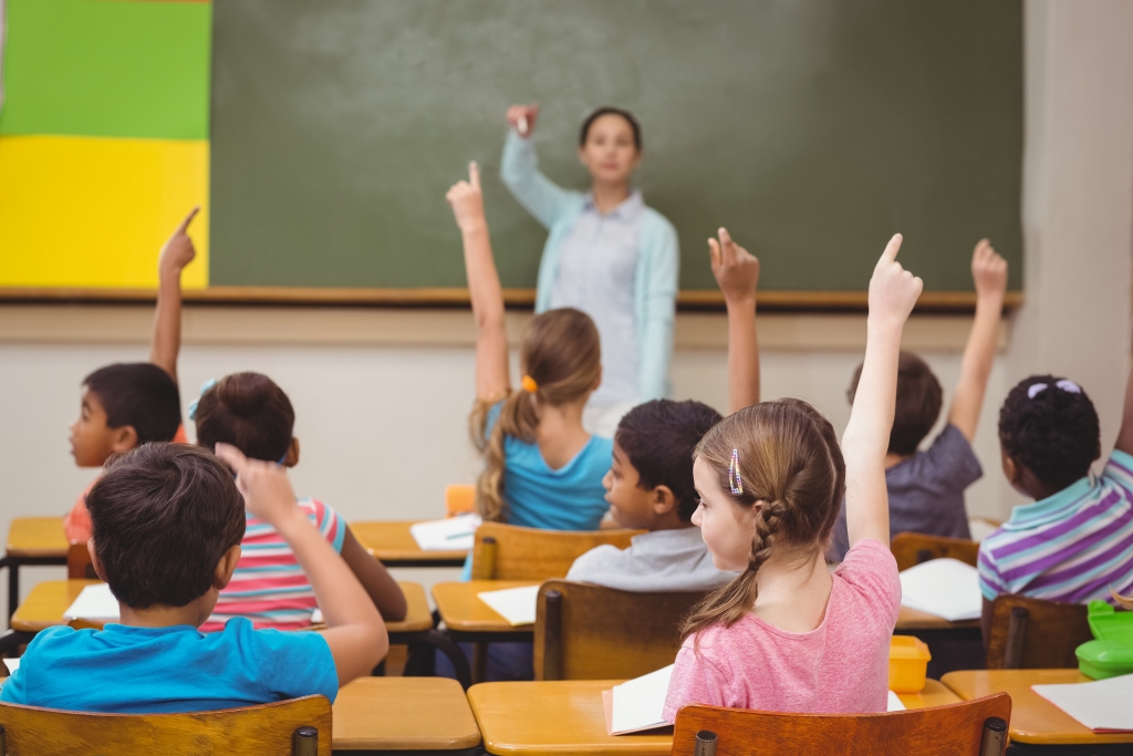 Teacher in a classroom full on children raising their hand