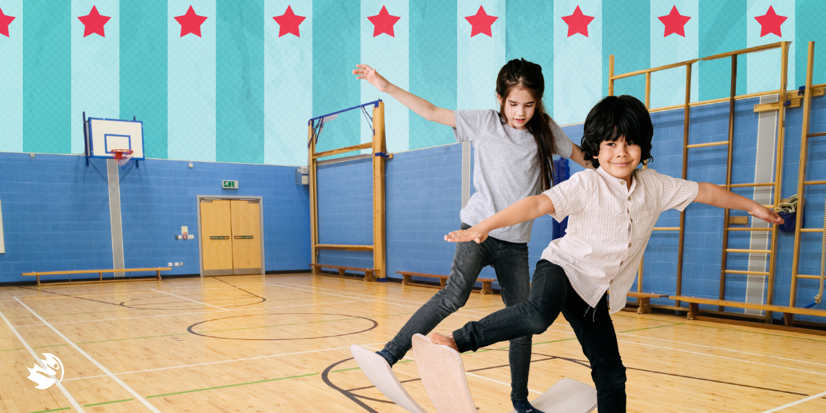 two students playing with balance board in a school gym.