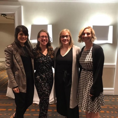 1. Four women standing together in a well-lit room, engaged in conversation and sharing smiles.