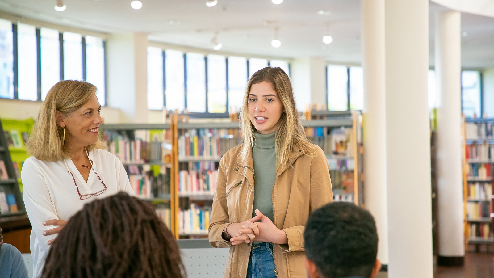 A woman engages with a group of individuals in a library setting, fostering discussion and collaboration among them.