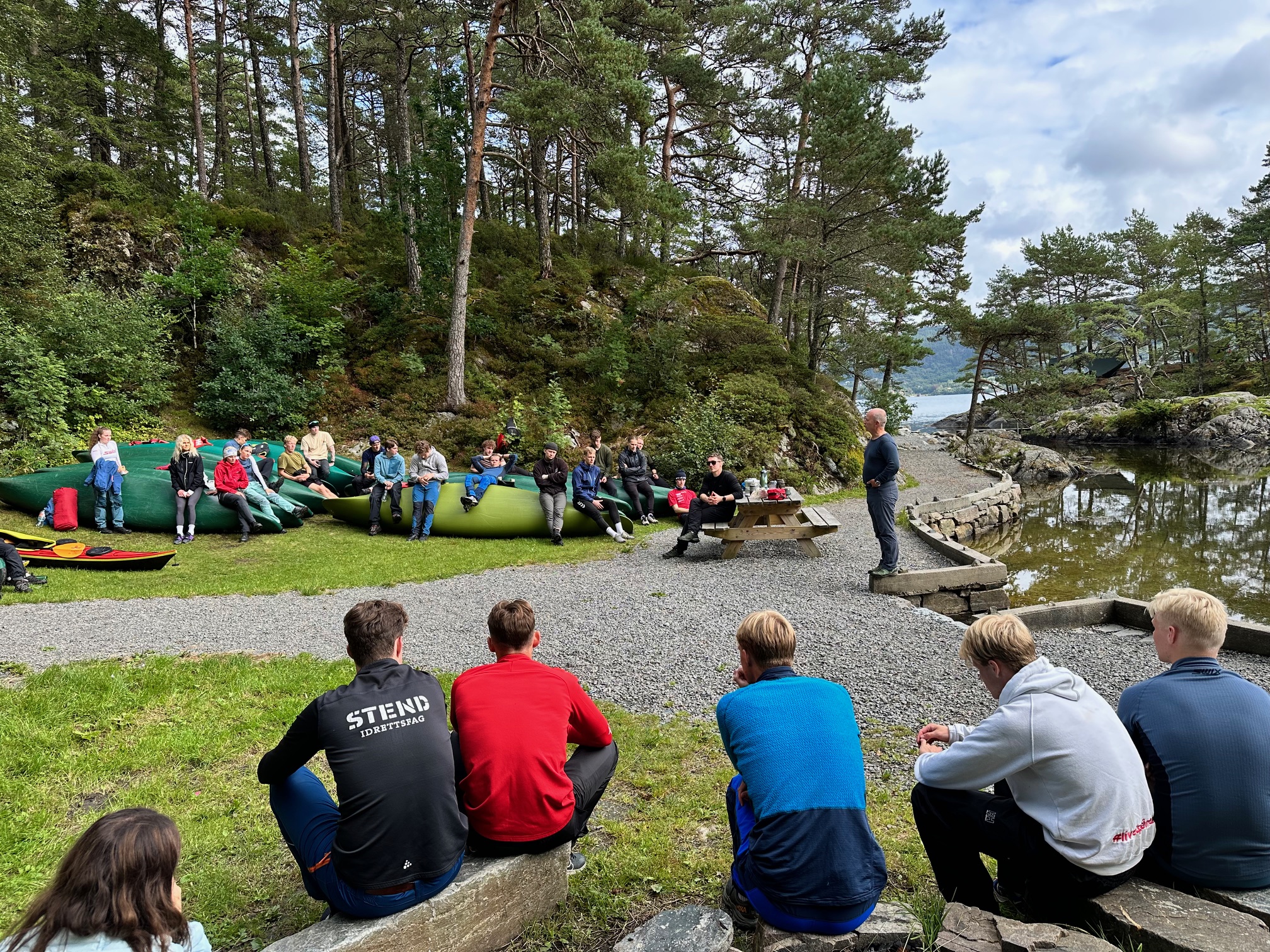 a photo showing a group of students listening to a teacher in an outdoor setting