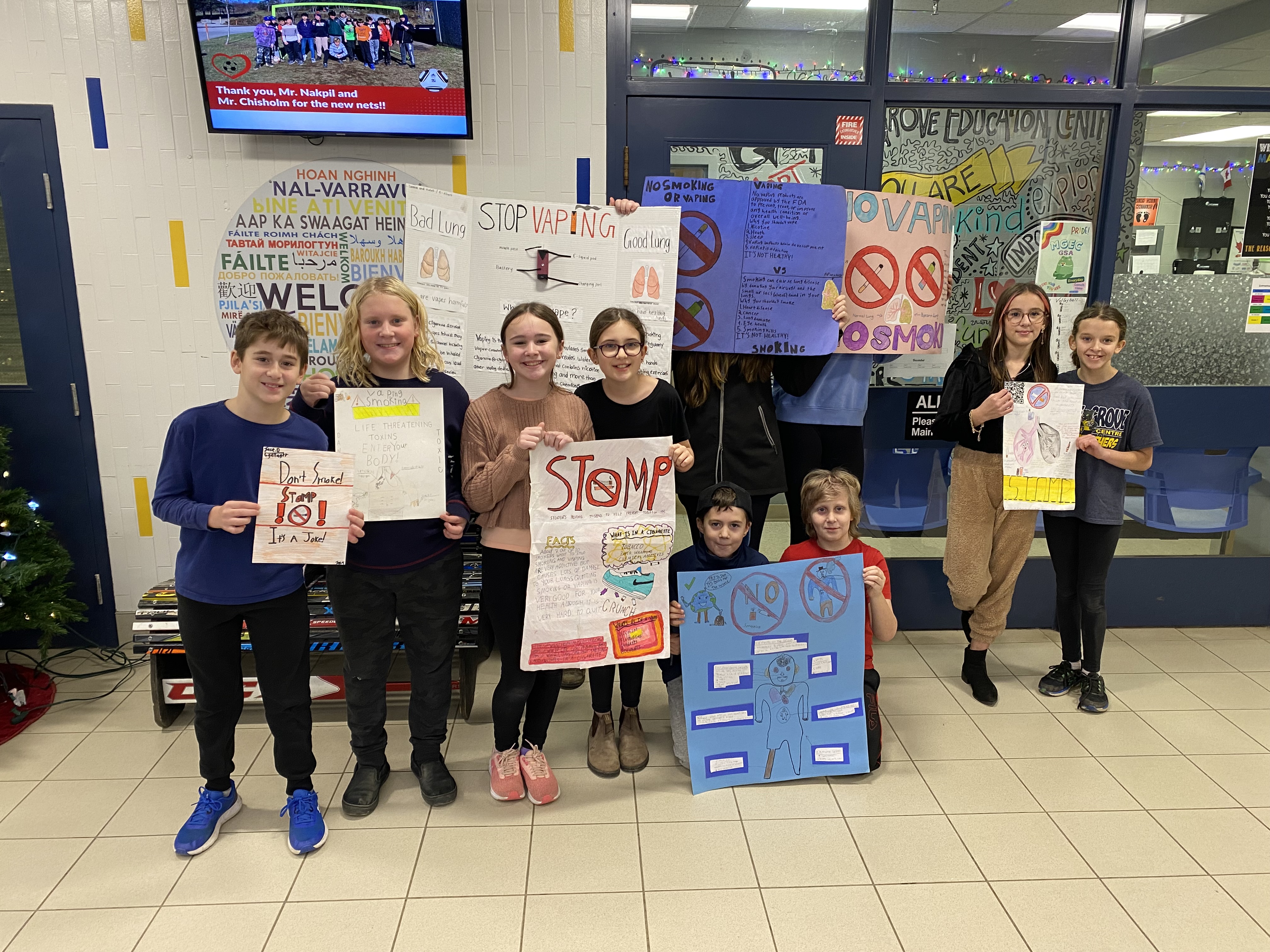 A group of children in a school holding colorful signs, smiling and engaging with their surroundings.