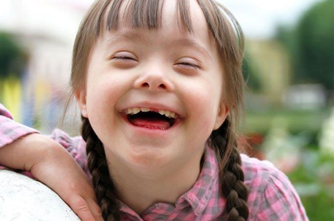 young girl with down syndrome smiling with a green field behind her