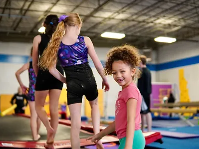 girl in a pink shirt nad green shorts at a trampoline doing gymnastics with two other girls