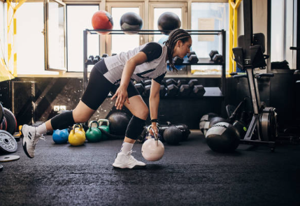 a young black women lifting a kettle bell in a weight room.