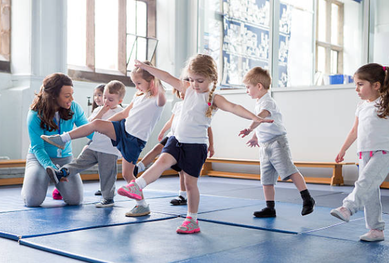 students in a dance studio with an instruction. They are young children trying dance moves. 