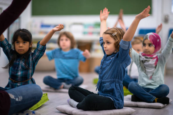 young students sitting on a pillow cross legged stretching with their arms in the air following the teacher