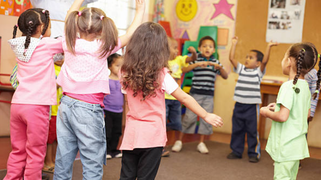 group of young children in a classroom standing in a circle dancing