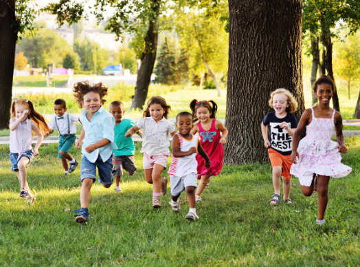 many young children running on grass past trees