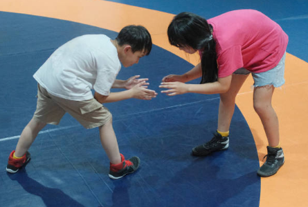 a young boy and young girl about to wrestle on a olympic wrestling mat