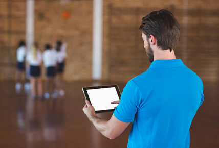 a teacher wearing a blue shirt holding an iPad while students are doing an activity
