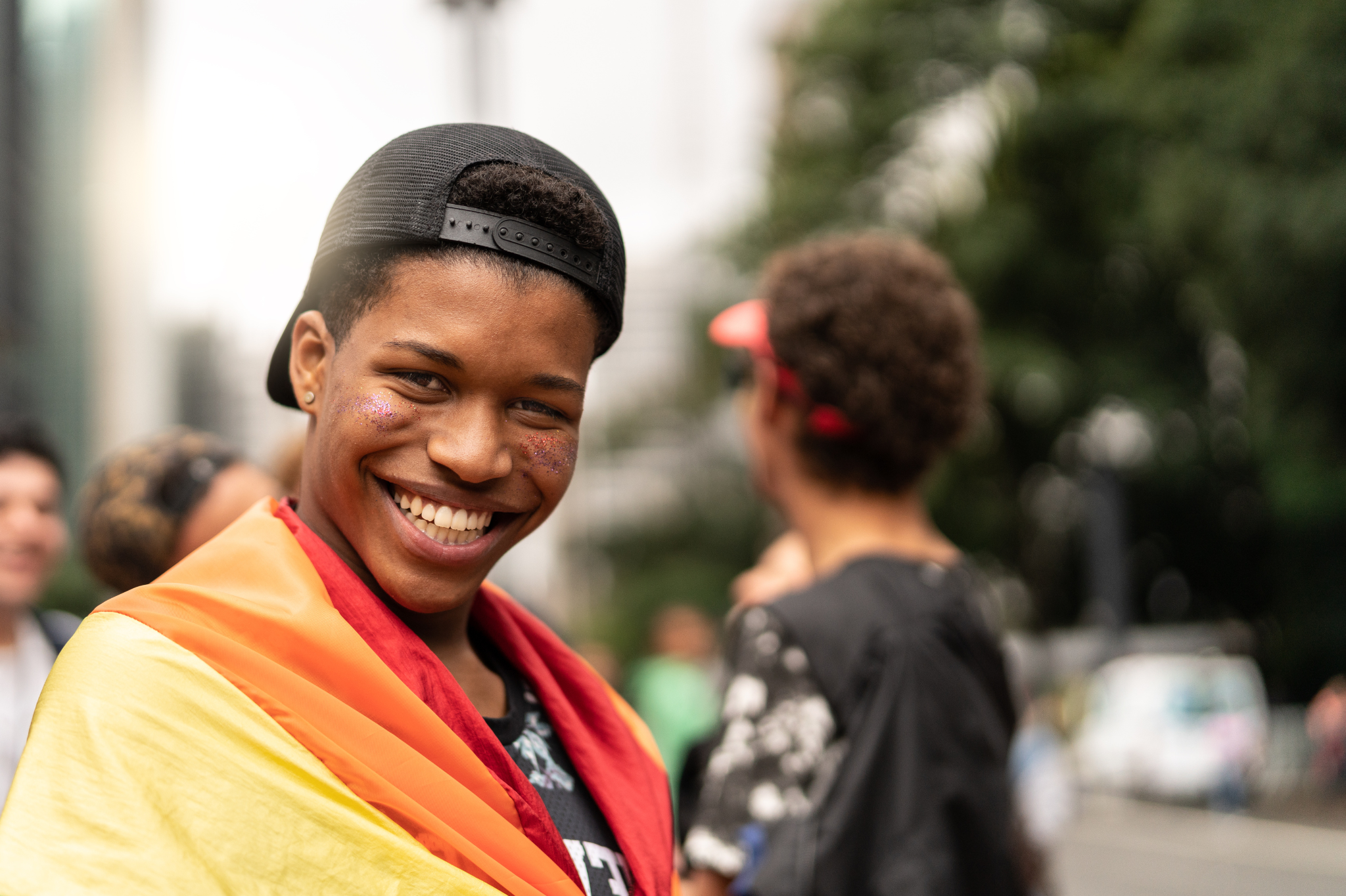 A young person carrying a rainbow flag and flashing an contagious, confident smile.