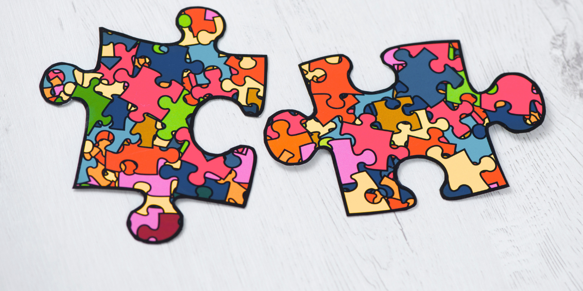 Two colorful puzzle pieces with a mosaic pattern of different shapes and colors on a light wooden background.