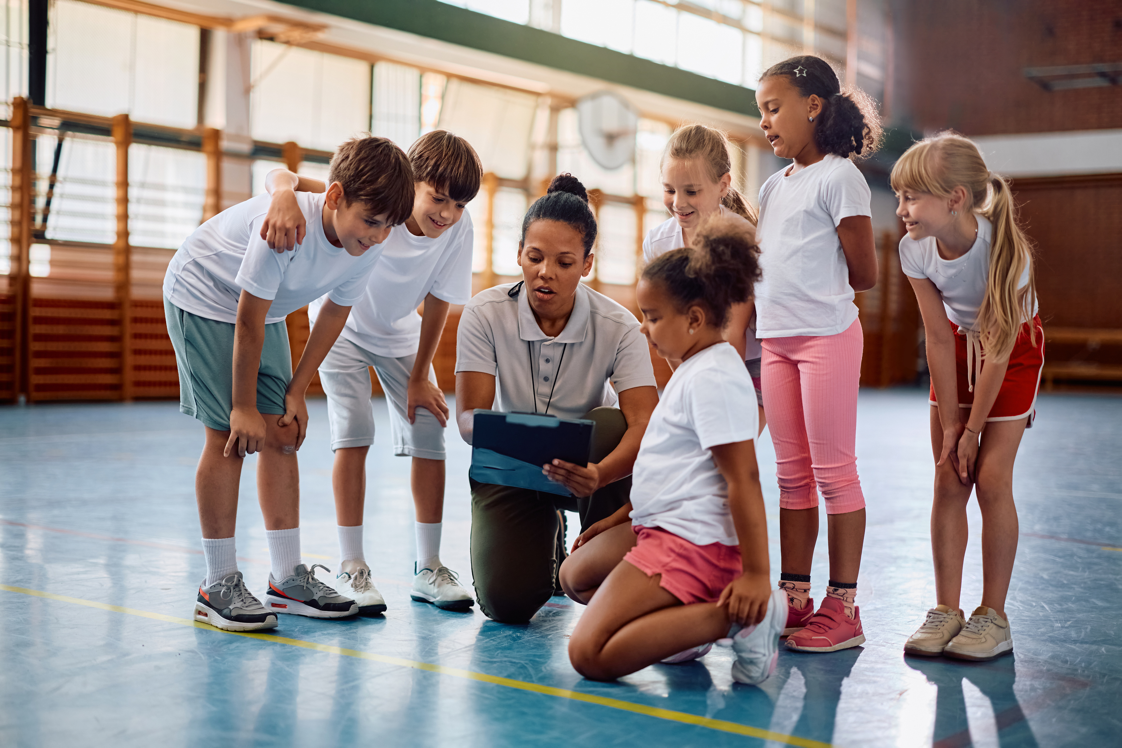 A teacher engages with a group of children in a gym setting, fostering interaction and learning.