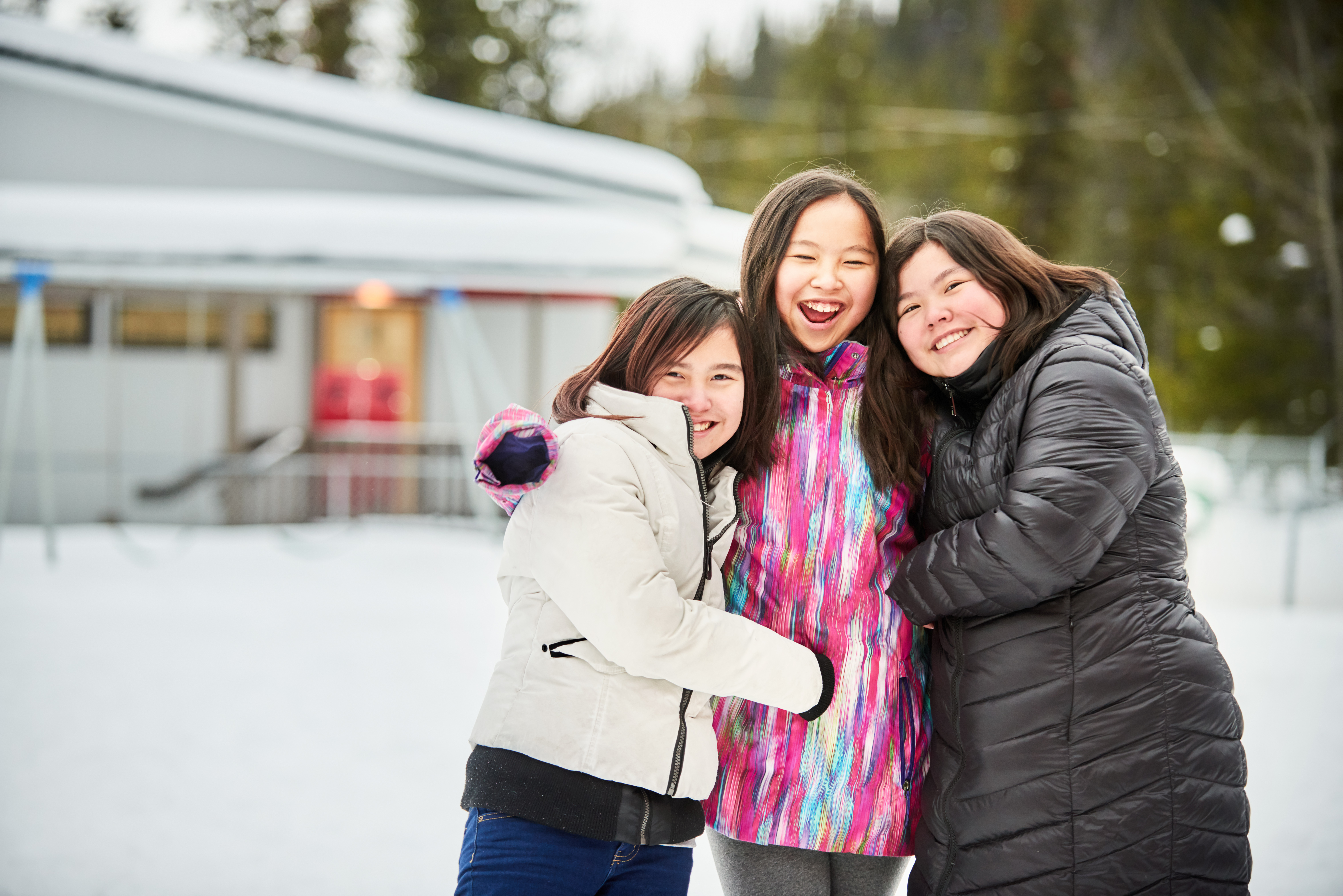 3 indigenous girls hugging and smiling while standing in the snow