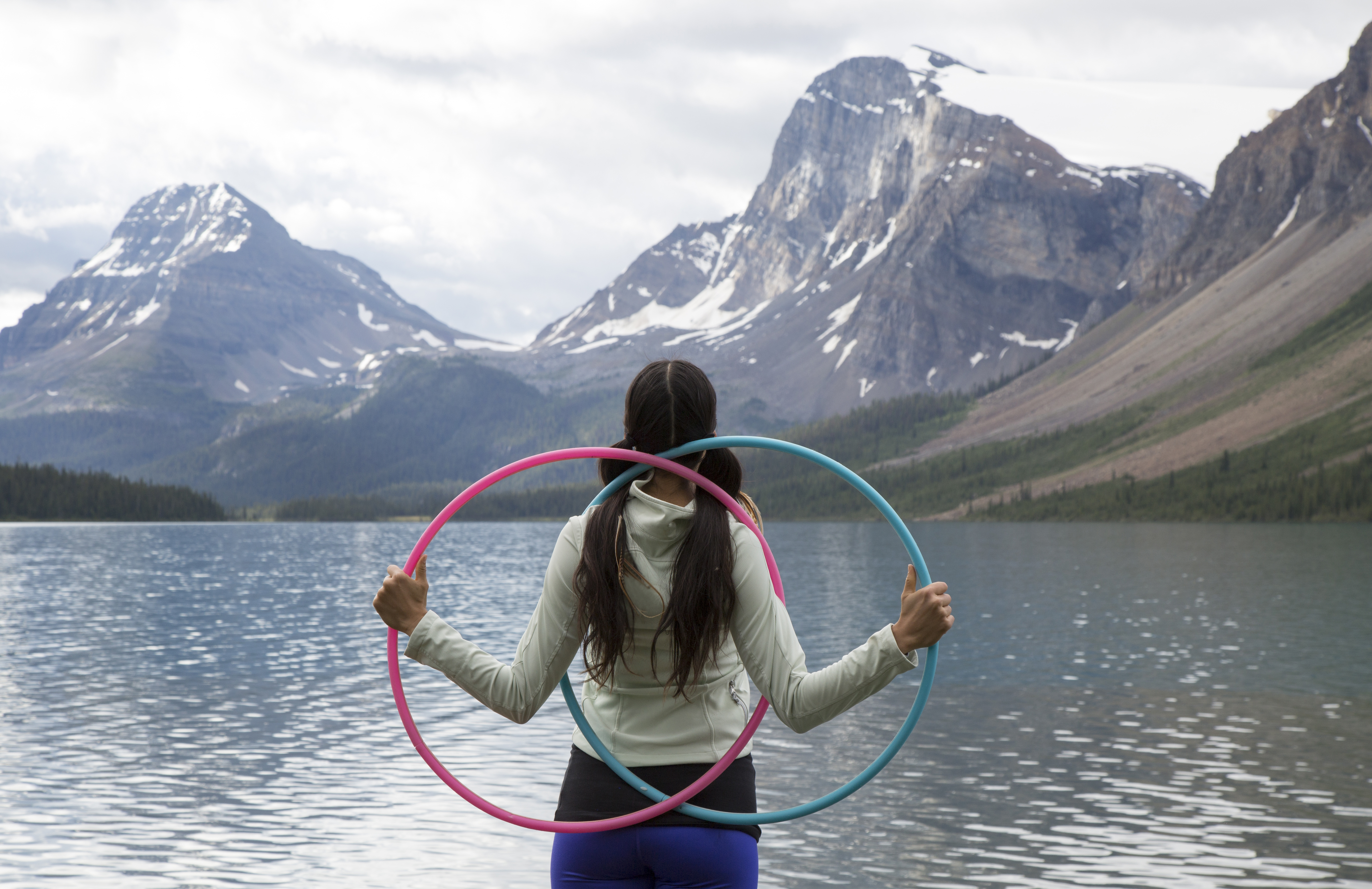 A young girl faces a mountain and carries two hoops.