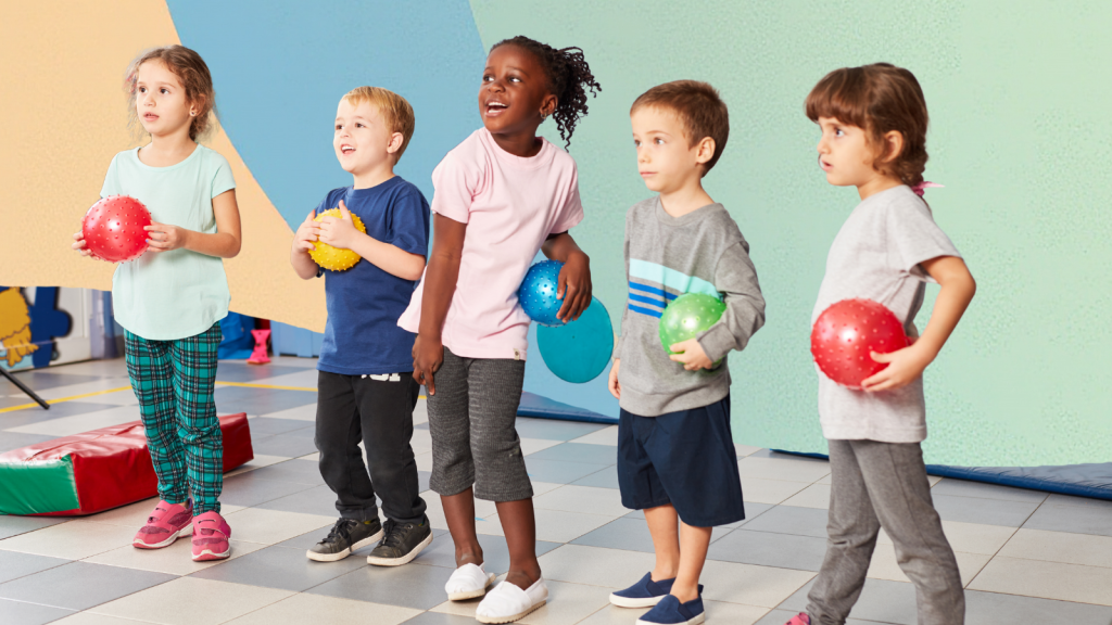 Five children of diverse backgrounds holding colorful balloons in a school gym.