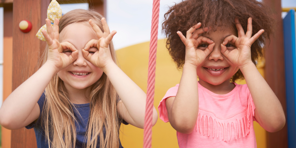 Two children making binoculars with their hands over their eyes while on a playground.