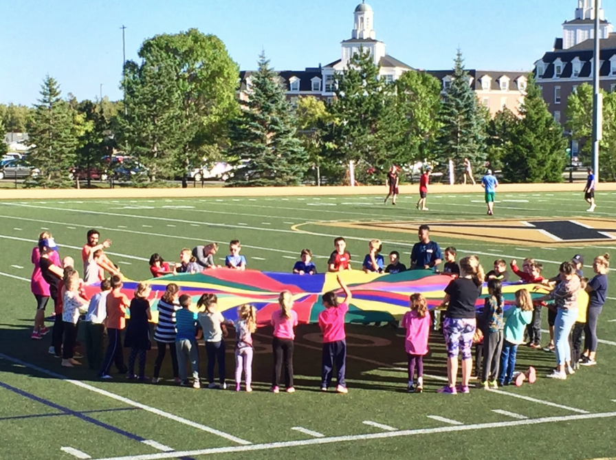 A group of students is playing parachute on a large open green space.