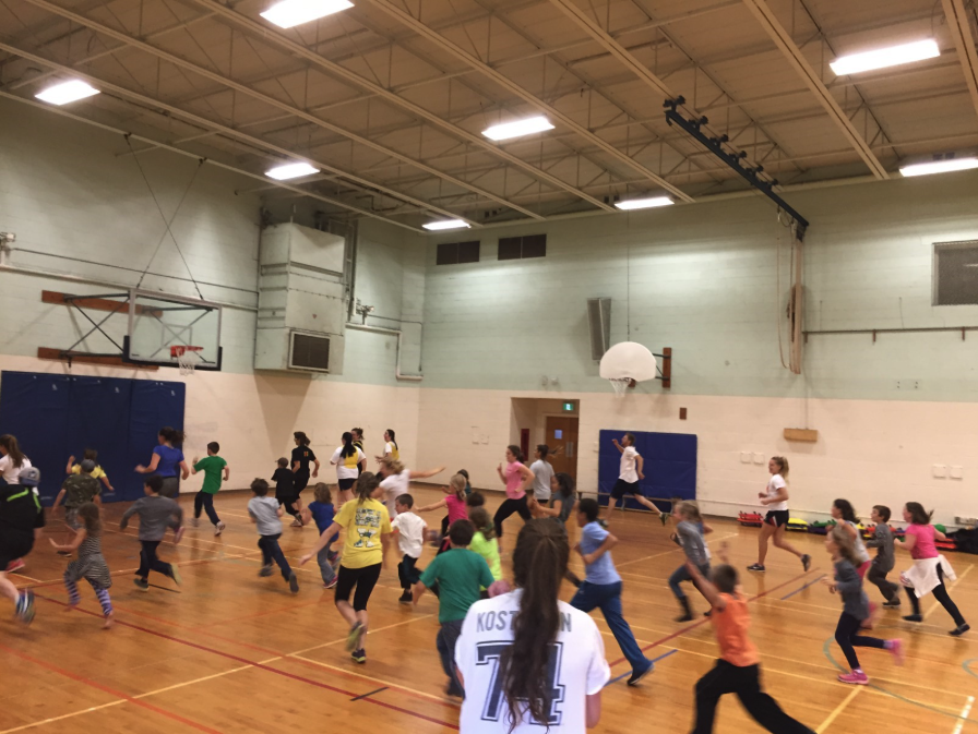 The photo is showing a group of children and educators running and moving in an indoor gym.