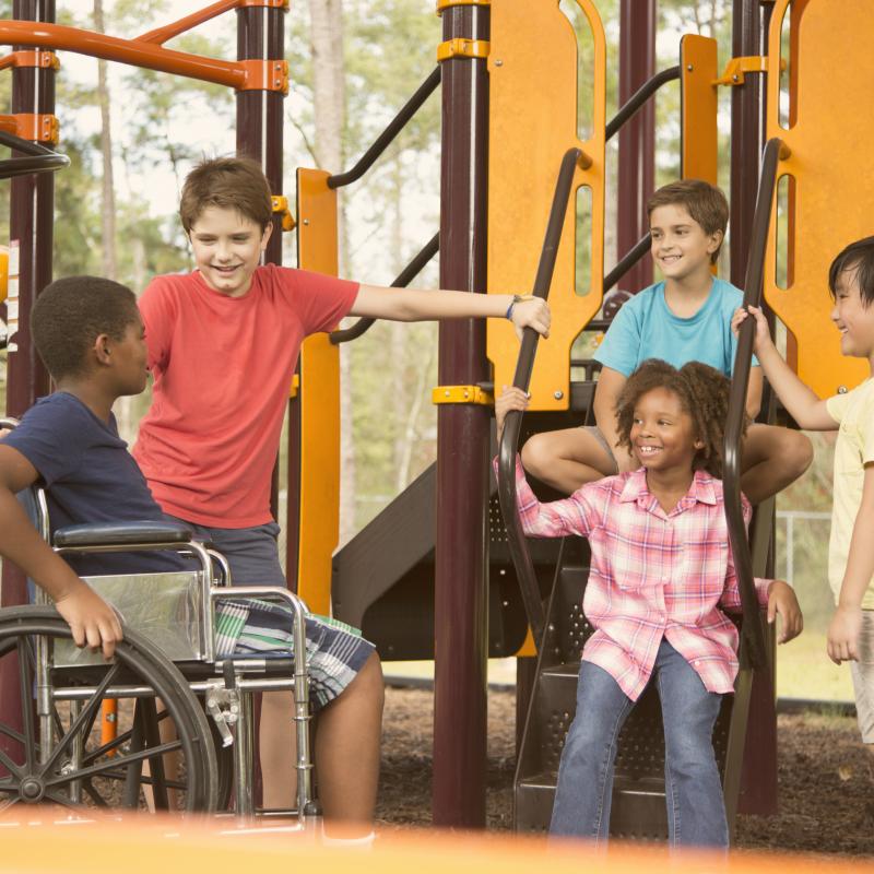 group of friends at a play structure on the ground with a child in a wheelchair