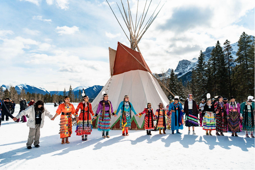 The photo shows a festive event taking place on snow-covered ground, celebrated by people dressed in traditional indigenous clothing.