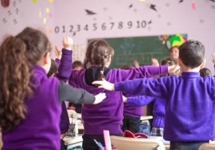 classroom of children wearing purple standing out of their chair doing a physical activity