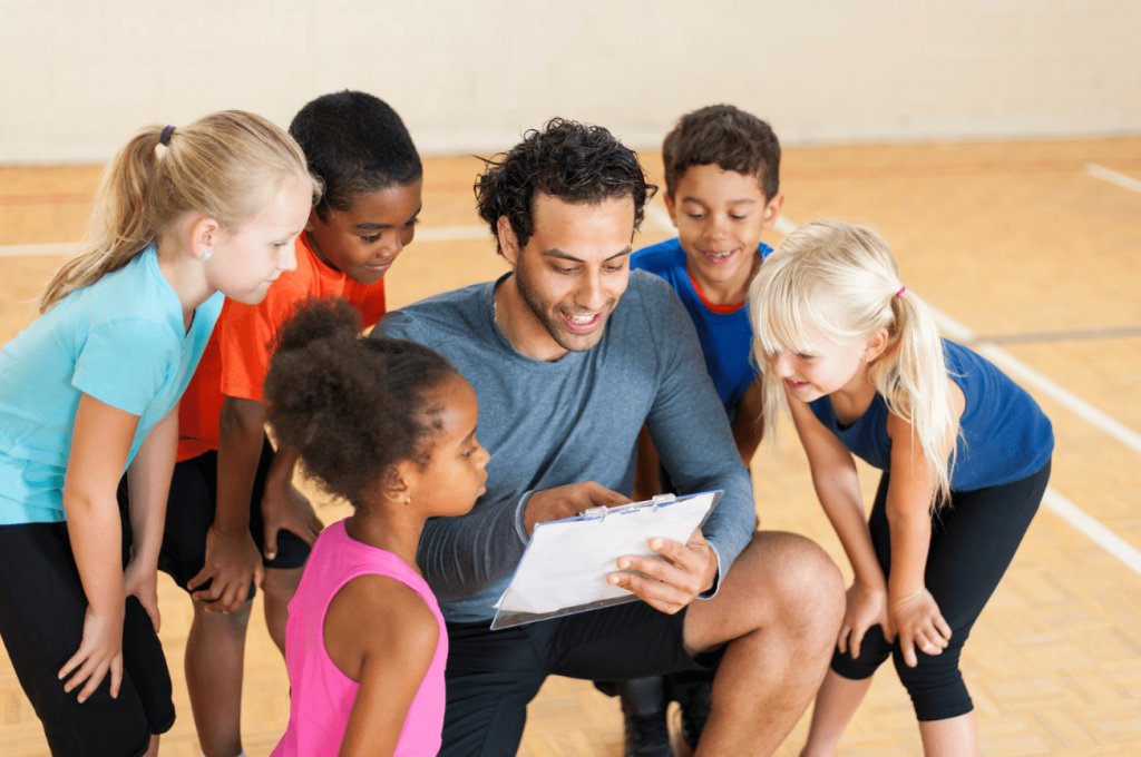 PHE teacher crouching, showing students something on a clipboard 