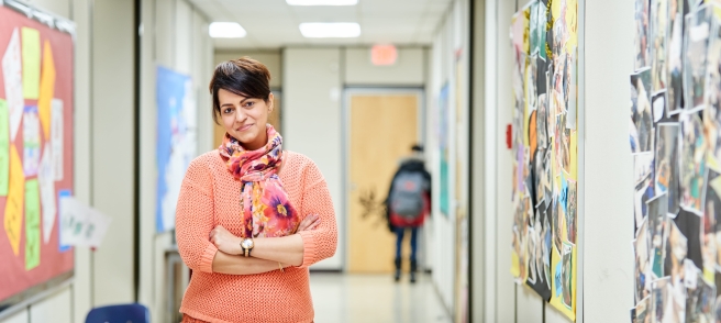 A woman stands in a hallway, arms crossed, exuding confidence and contemplation in her posture.
