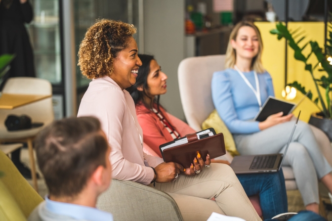 A diverse group of individuals engaged in discussion around a conference table in a meeting room.
