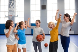 A joyful group of children and adults celebrating their victory after a basketball game, smiling and cheering together.