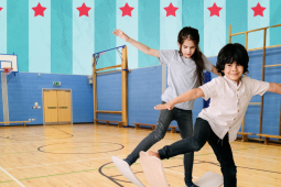 two students playing with balance board in a school gym.