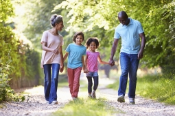 a Black family walking on a trail outside. There is a mother, father and two young girls between them. They are all holding hands.