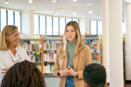 A woman engages with a group of individuals in a library setting, fostering discussion and collaboration among them.