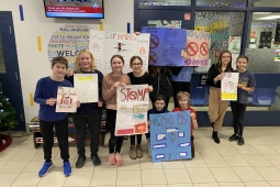 A group of children in a school holding colorful signs, smiling and engaging with their surroundings.