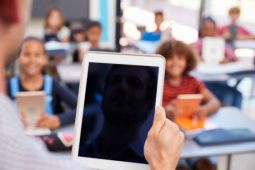 a teacher holding up a blank iPad screen in front of the class of students. 