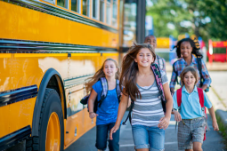4 children getting off of a school bus walking and smiling. 