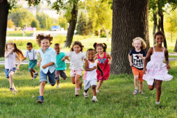 many young children running on grass past trees