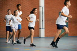 5 children wearing white t-shirts running in a gymnasium following one another