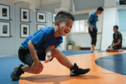 a young boy stretching his leg on a wrestling mat