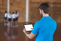 a teacher wearing a blue shirt holding an iPad while students are doing an activity