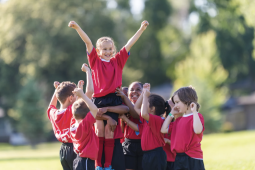 a group of kids outdoors in uniforms holding up a girl in celebration 