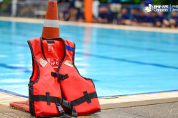The photo shows a lifejacket lying next to a safety cone next to a swimming pool