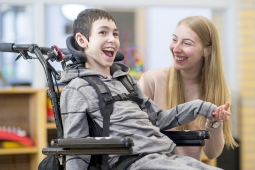young boy in a wheelchair with an adult holding his hand