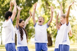 A group of children joyfully playing soccer in a sunny park, with trees and grass in the background.