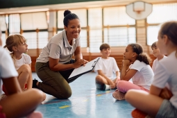 A teacher engages with a group of children in a gym setting, fostering interaction and learning.