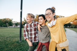 A group of three school-age children can be seen walking together outside a school. They appear happy and are clearly enjoying each other's company.