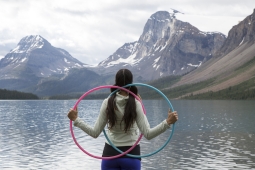 A young girl faces a mountain and carries two hoops.