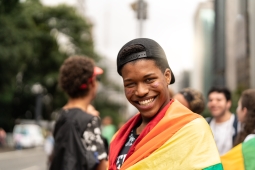 A young person carrying a rainbow flag and flashing an contagious, confident smile.