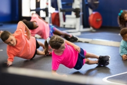 5 children in a weight lifting room on their sides holding a side plank exercise